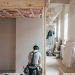 A general contractor kneeling before a wall frame in a house.