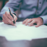 A close-up shot of a person at a desk signing a contract.