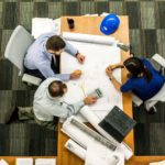 Three people sit around a table and assess the logistics of an upcoming construction project.