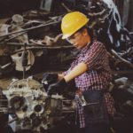 A person working in the construction trades wearing a plaid shirt, tool belt, and hard hat while operating a table saw.