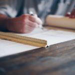 A person sits at a desk with a ruler on it and works drawing up a construction plan with a pen