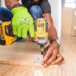 Handyman using yellow drill bracket on shelf on hardwood floor.