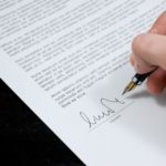 A closeup of a person signing a contract.