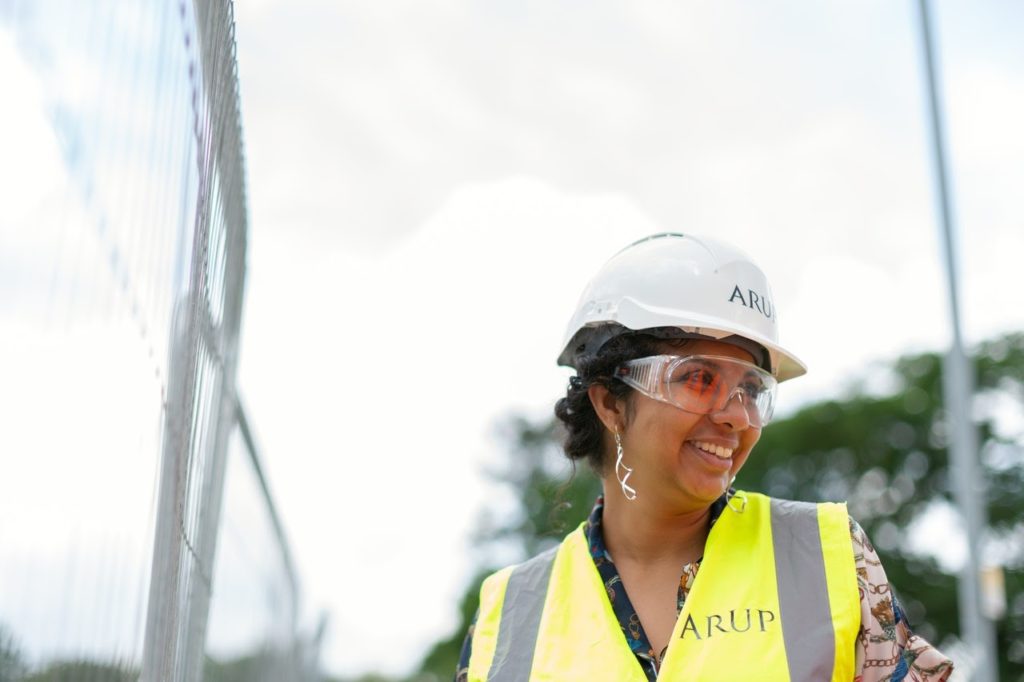 An engineer in a hard hat and safety vest smiling on a construction site.